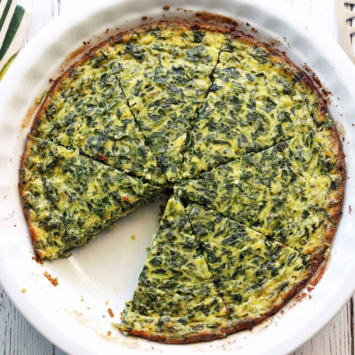 Crustless spinach quiche is served in a white pie plate.