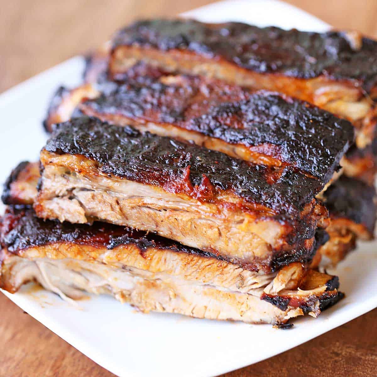 Oven-baked spare ribs are stacked on a white plate.