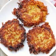 Three latkes are served on a white plate.