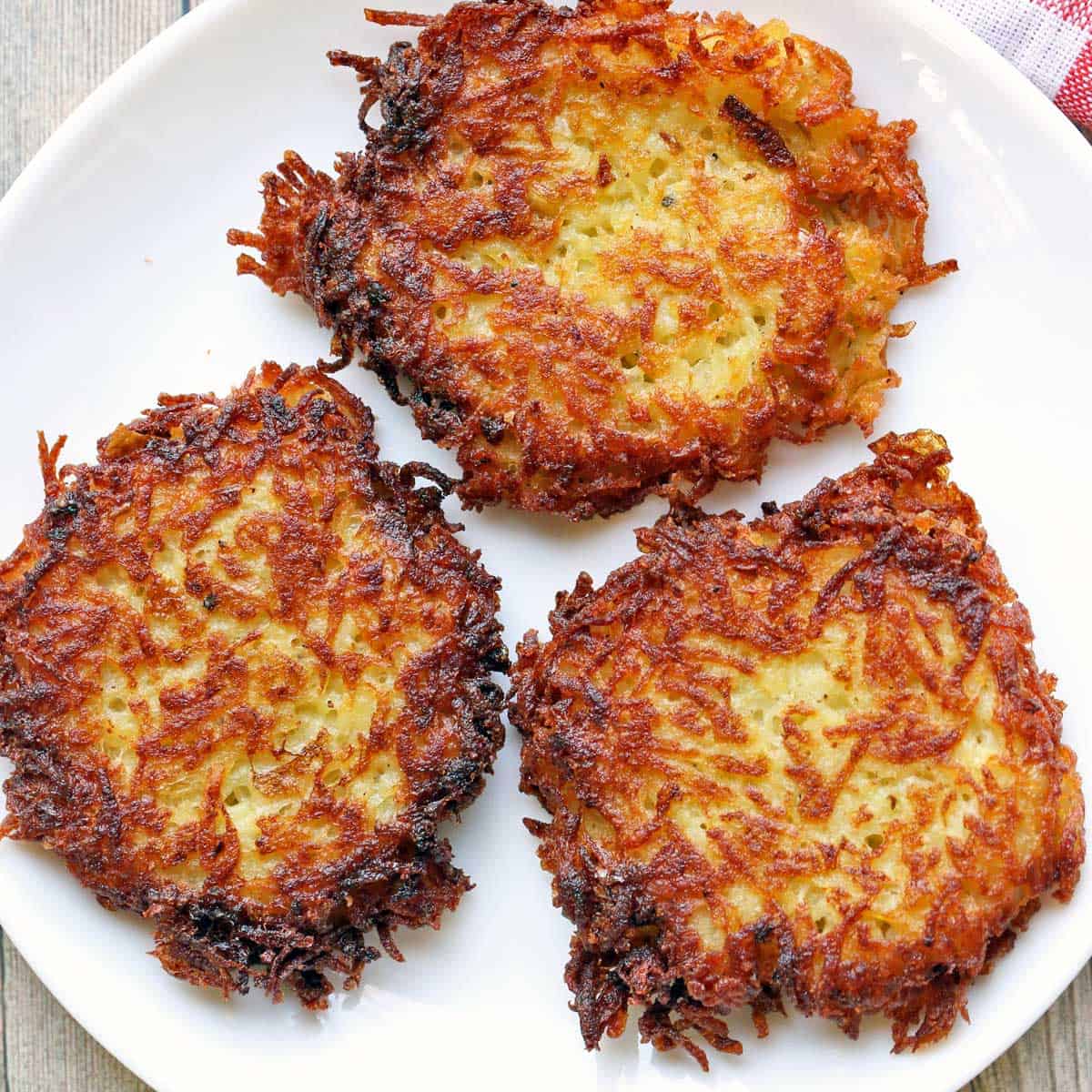 Three latkes are served on a white plate.