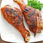Turkey legs are served on a white plate with a garnish of parsley.