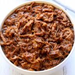 Slow cooker pulled pork is served in a white bowl.