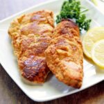 Keto fried fish is served with lemon slices and parsley.