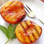 Grilled peaches are served on a white plate with a fork.