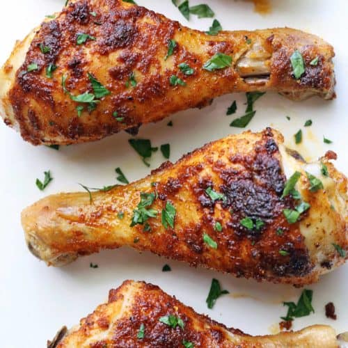 Baked chicken drumsticks are served on a white plate.