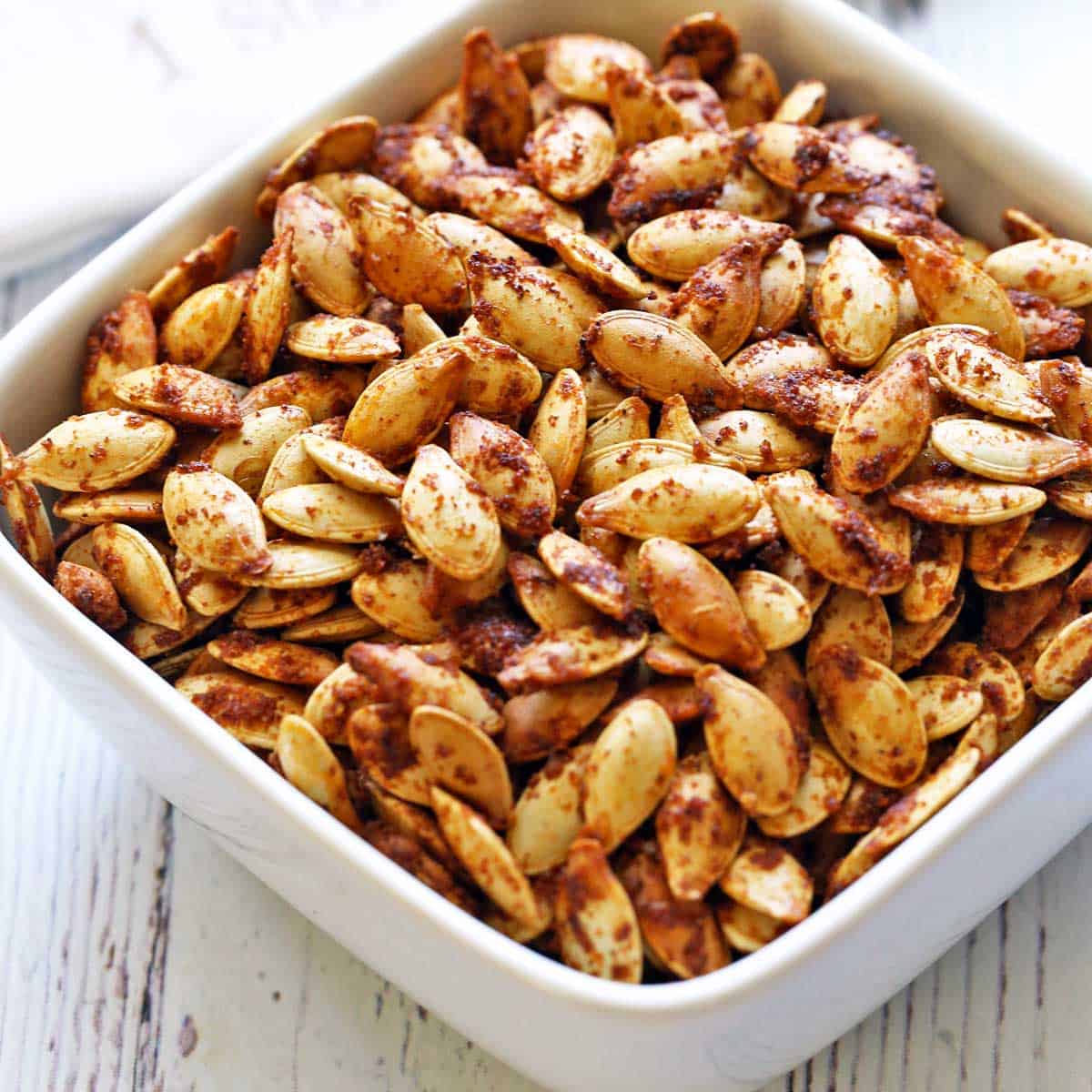 Roasted pumpkin seeds are served in a white bowl.