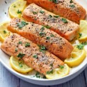 Baked salmon is served on a platter with lemon slices.