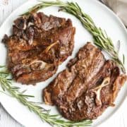 Lamb shoulder chops are served on a white plate with a garnish of rosemary.