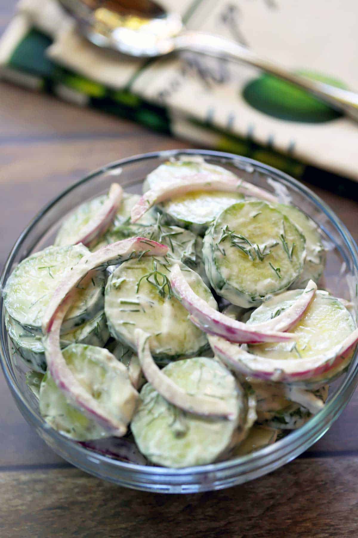 Creamy cucumber salad with onions, dill and sour cream, 
 is served in a glass bowl.