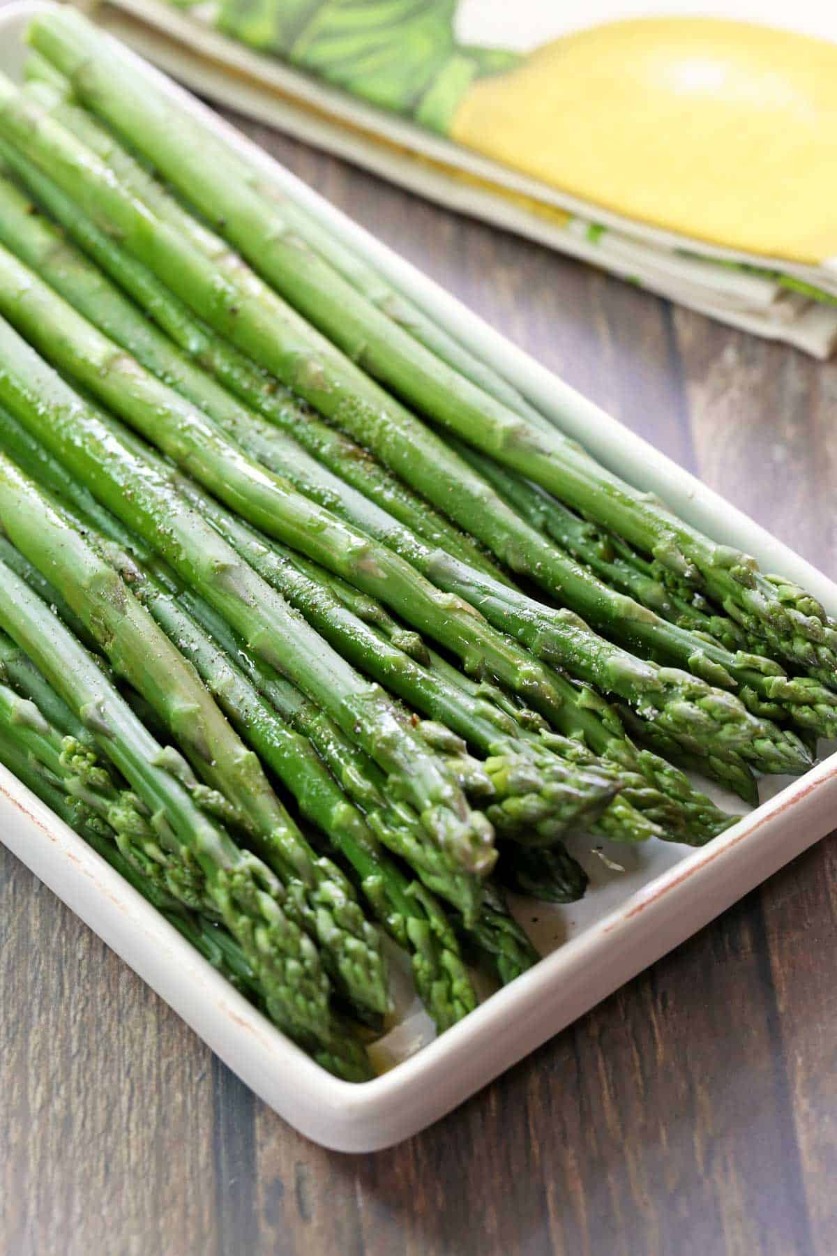 Steamed asparagus is served on a white serving tray.