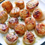 Seared scallops are served on a white plate.
