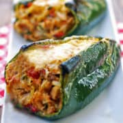 Stuffed poblano peppers are served on a white plate with a napkin.