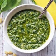 Homemade pesto sauce is served in a white bowl with a spoon.
