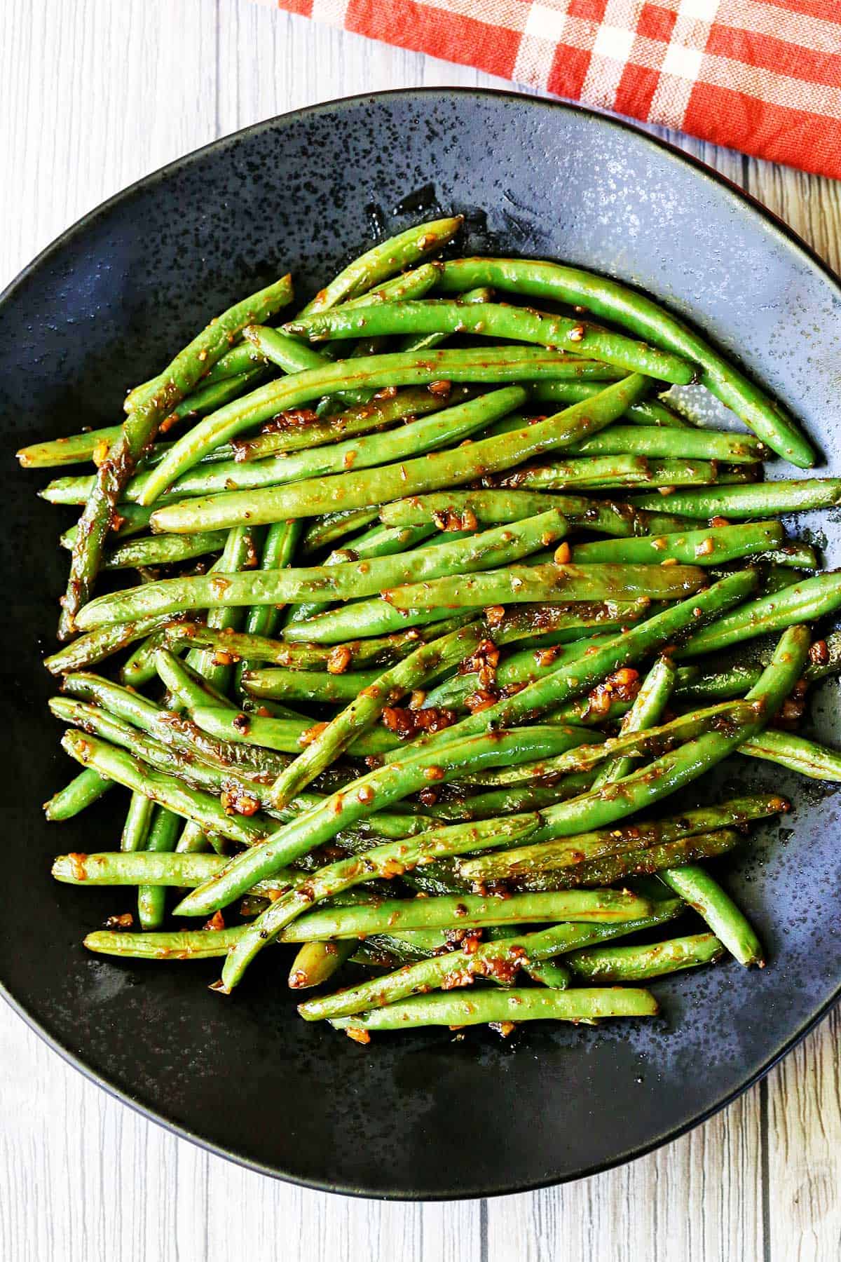 Spicy green beans are served on a black plate with a red napkin.