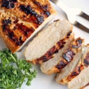 Grilled chicken breast, sliced, is served on a white plate.