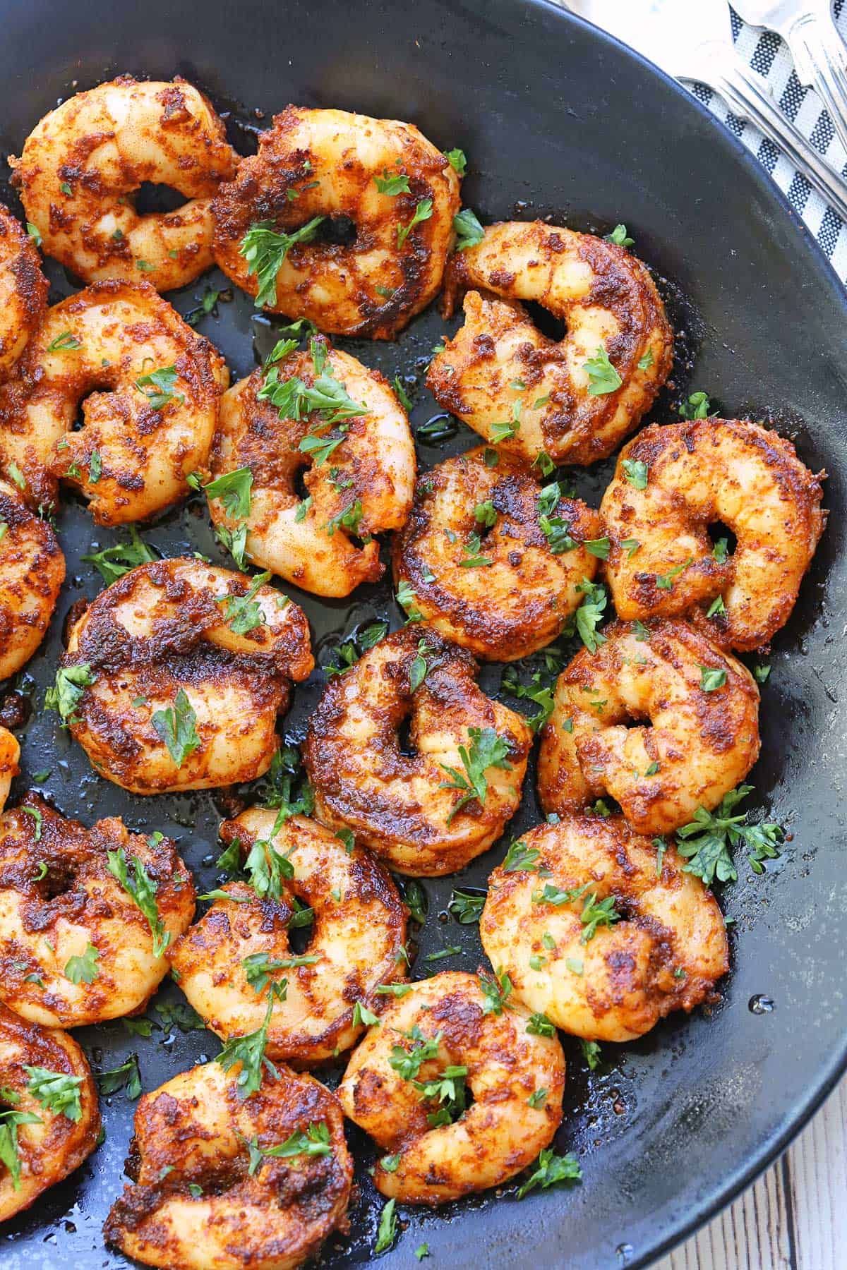 Spicy shrimp are served on a black dinner plate, garnished with parsley. 