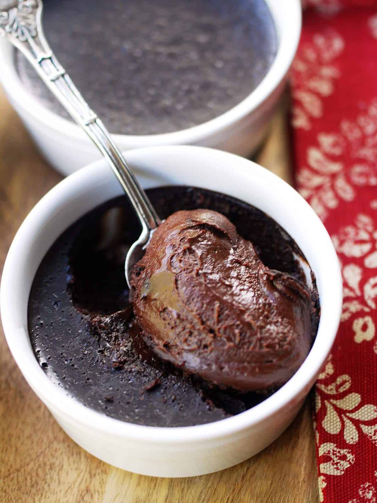 A spoon is showing off the creamy texture of a homemade baked chocolate custard. 