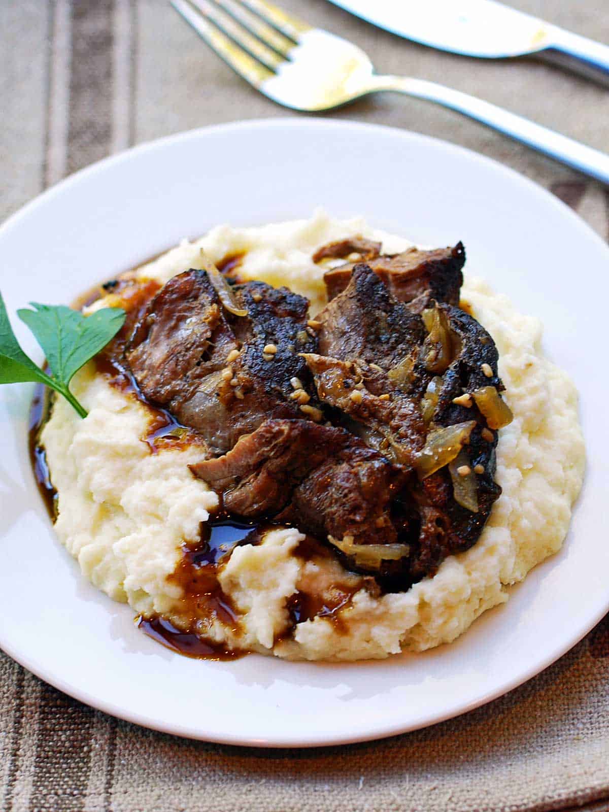 Keto pot roast is served on a bed of mashed cauliflower. 
