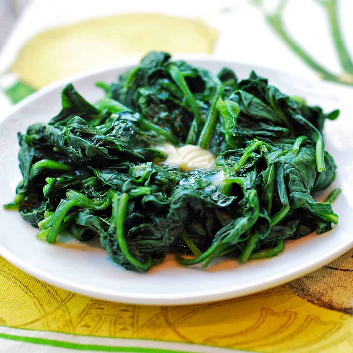 Steamed spinach is topped with a pat of butter.