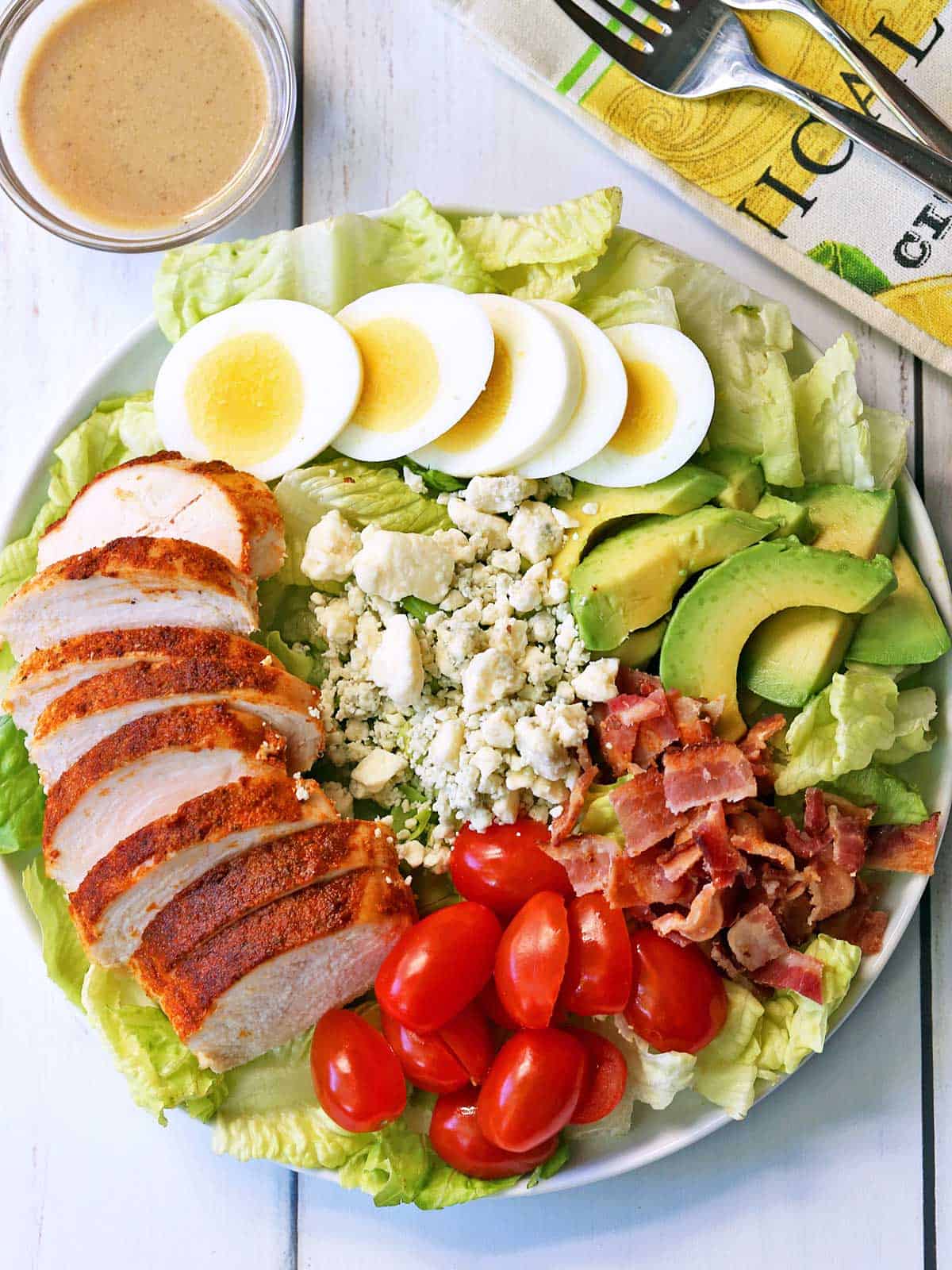 Cobb salad is served on a white plate with a napkin and dressing on the side. 