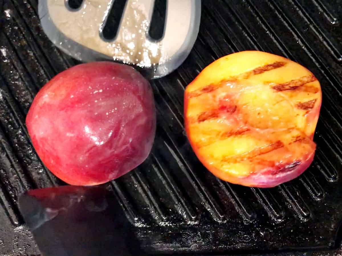 A peach cut in half being grilled on a grill pan.