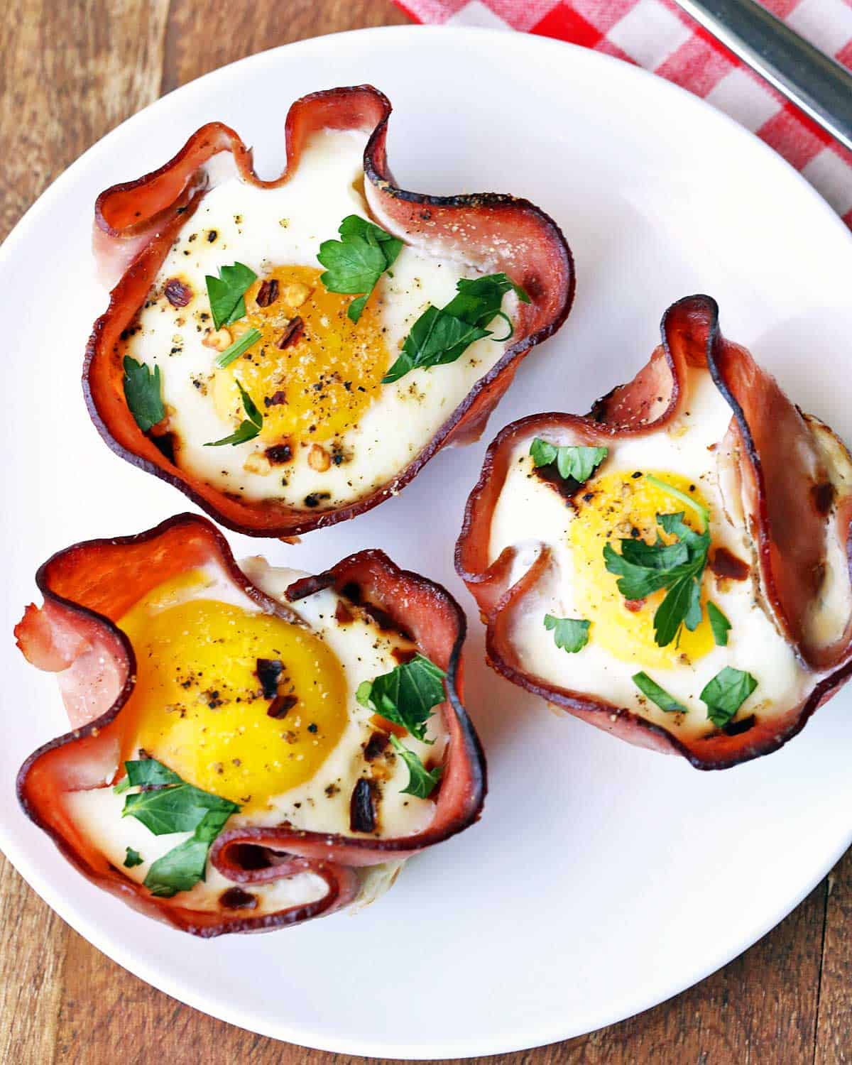 Three ham and egg cups are served on a white plate. 
