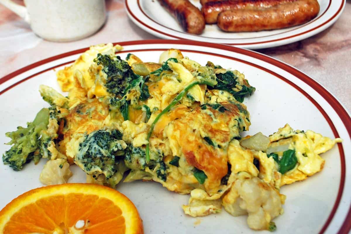 A veggie scramble served with sausages and a slice of orange.
