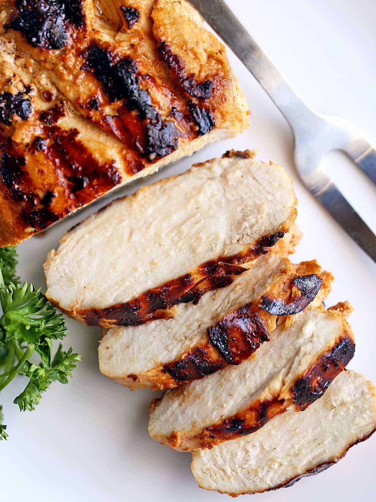 Grilled chicken breast served on a white plate with a serving fork. 