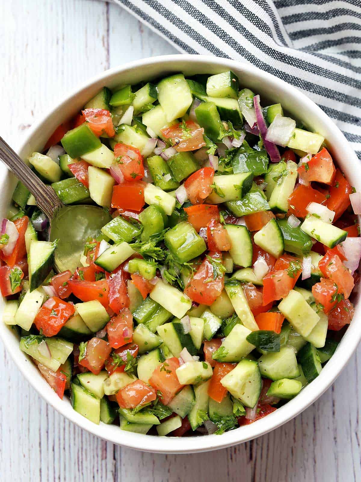 Israeli salad is served in a white bowl with a striped napkin. 