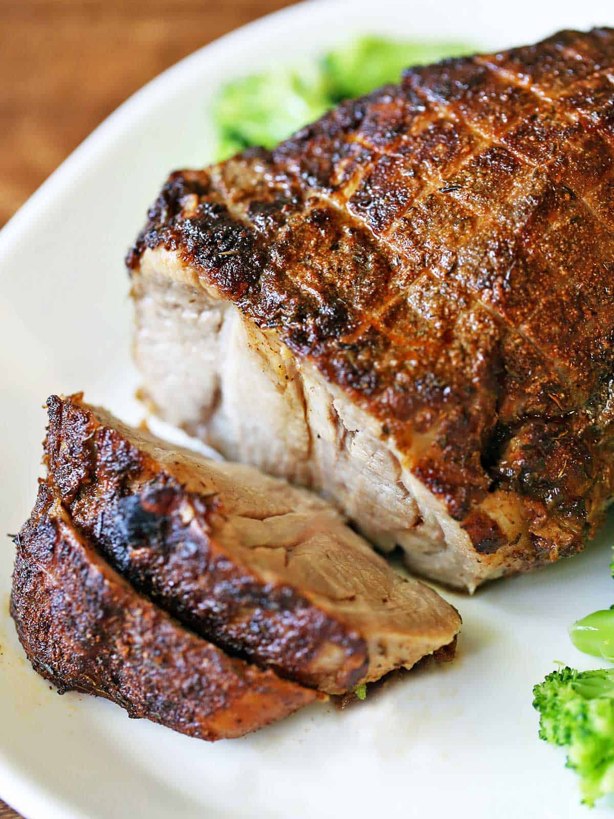 Pork roast is served on a white platter with veggies.