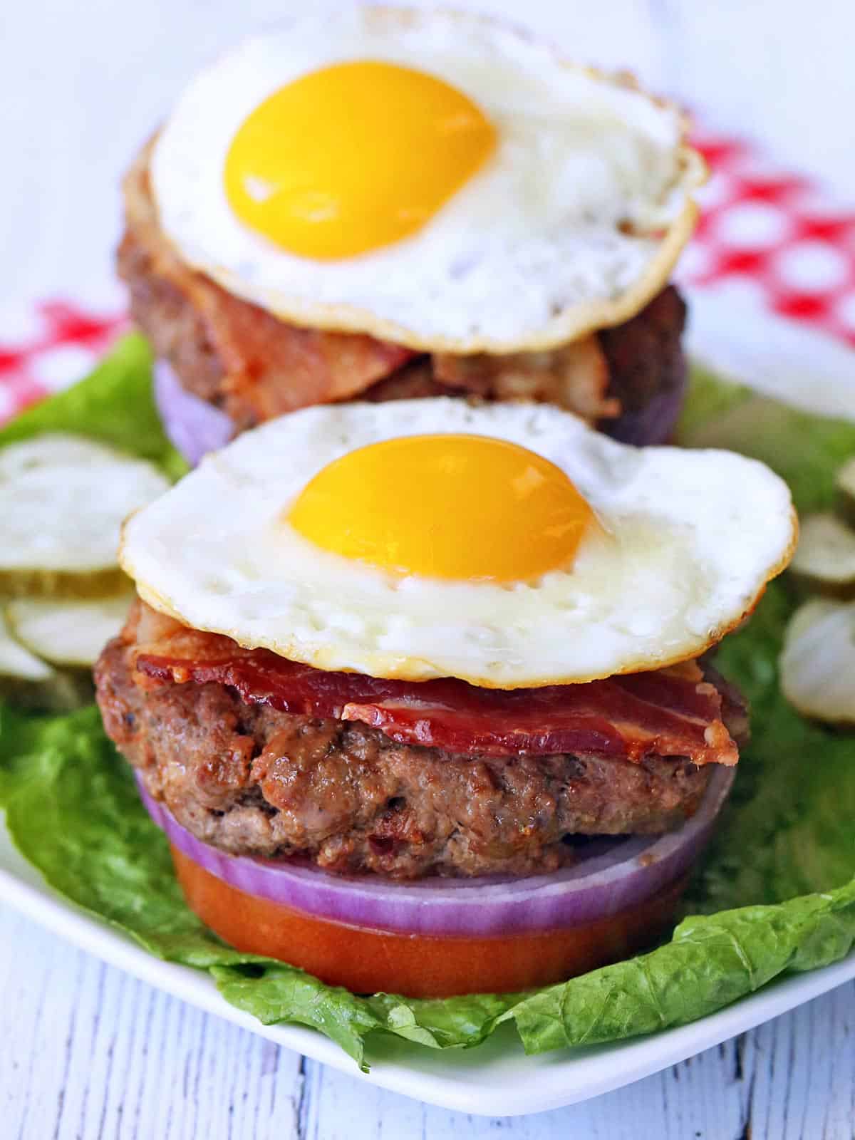 Two bacon burgers are topped with fried eggs.