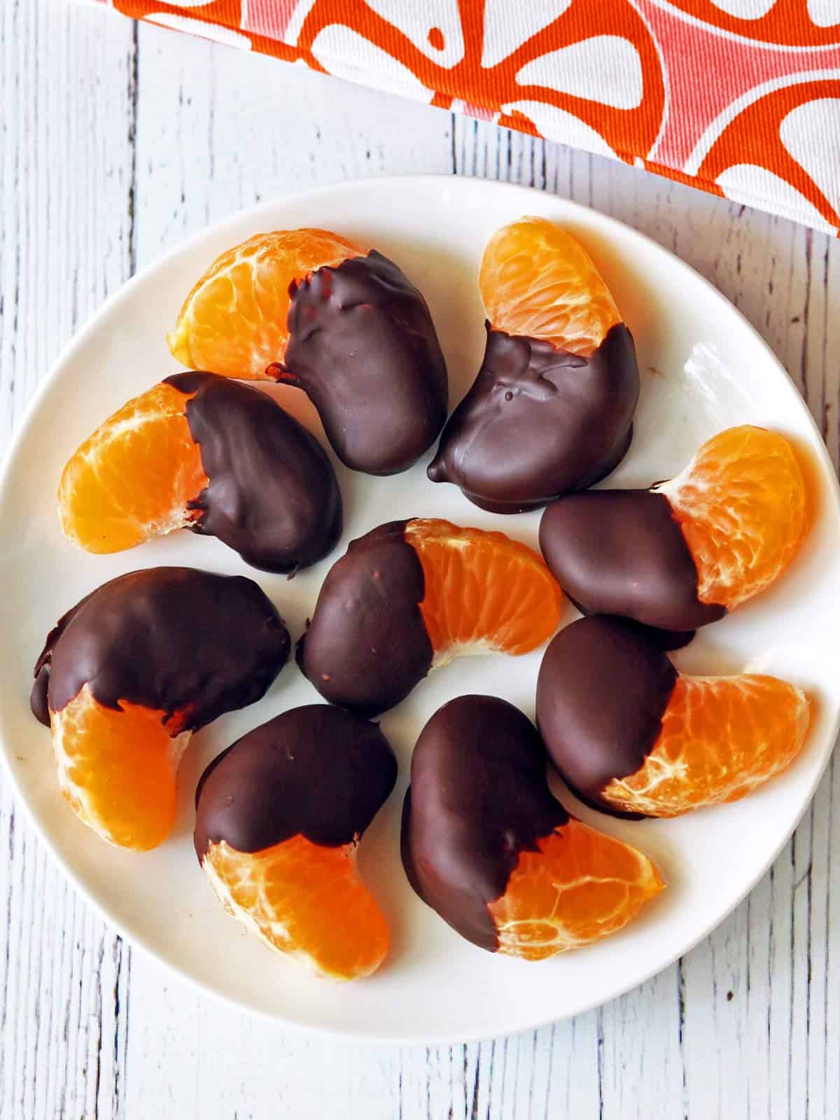 Chocolate covered oranges are served on a white plate.