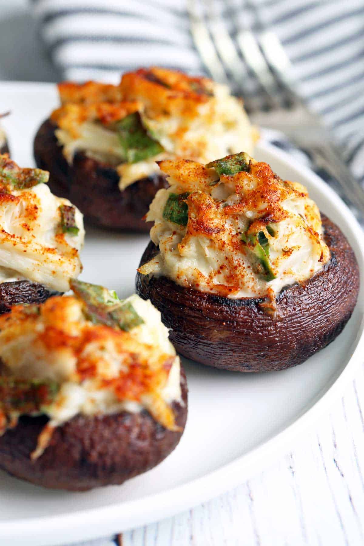Crab-stuffed mushrooms are served on a white plate.