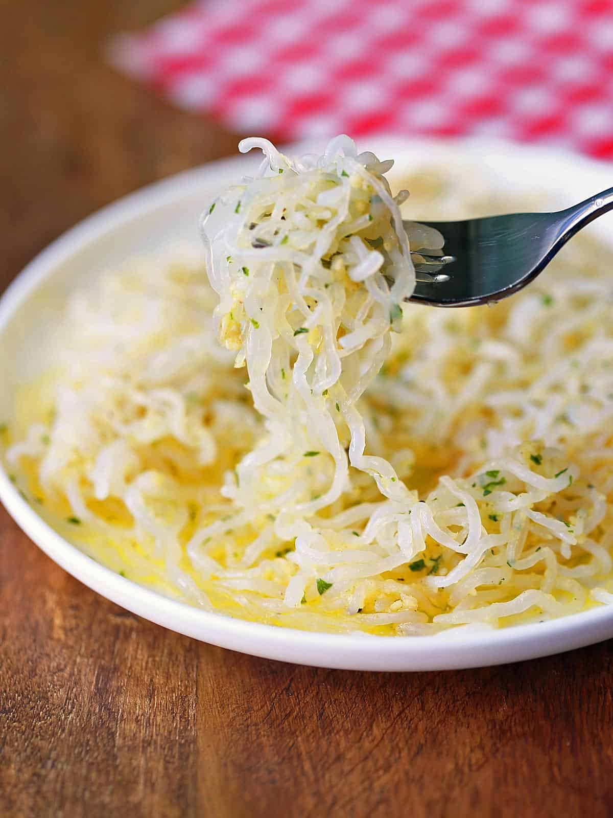 Shirataki noodles are served on a white plate and eaten with a fork.