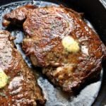 Two ribeye steaks are topped with butter and served in a cast-iron skillet.