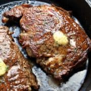 Two ribeye steaks are topped with butter and served in a cast-iron skillet.