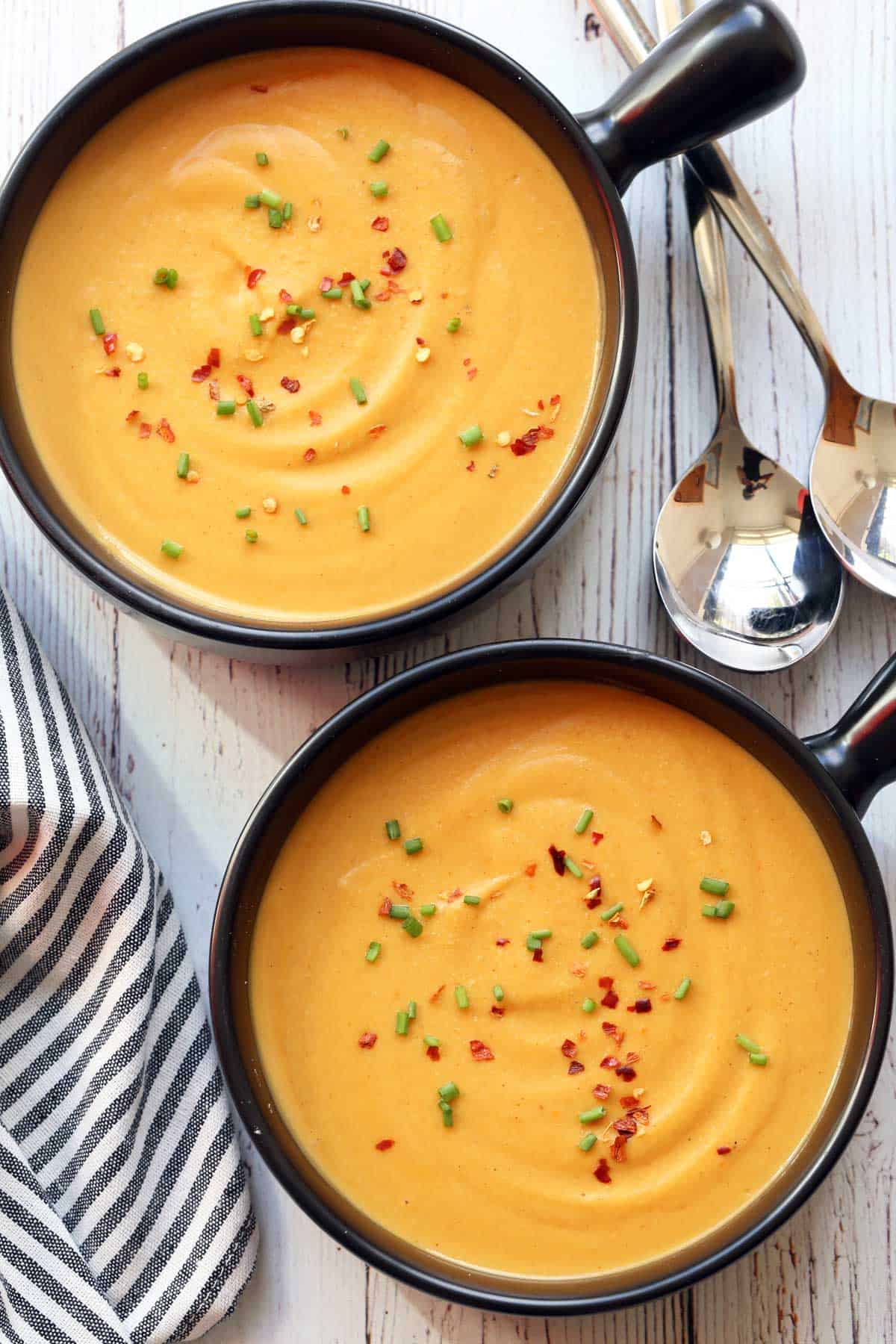 Butternut squash soup is served in two black bowls.