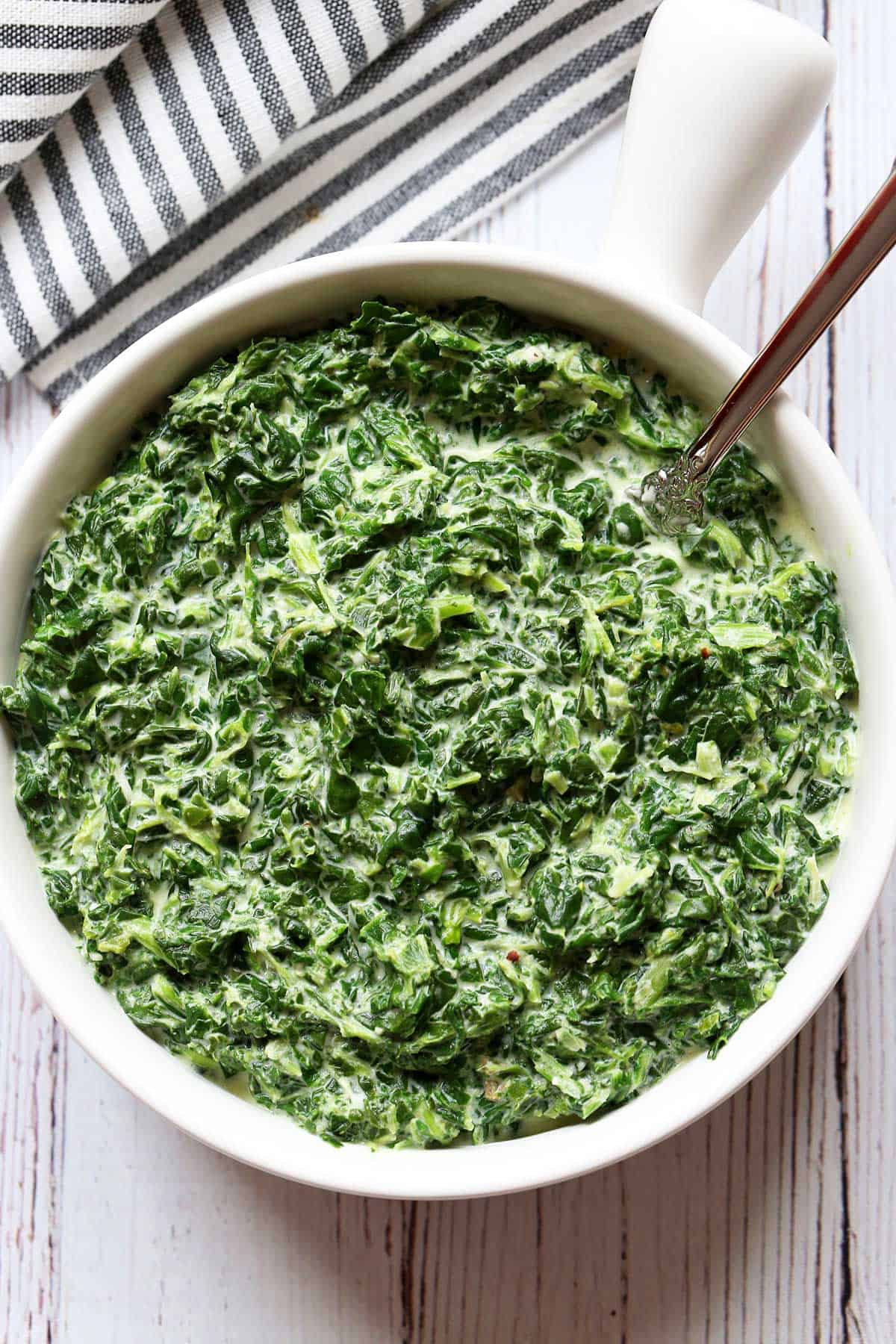 Creamed spinach is served in a white bowl with a spoon. 