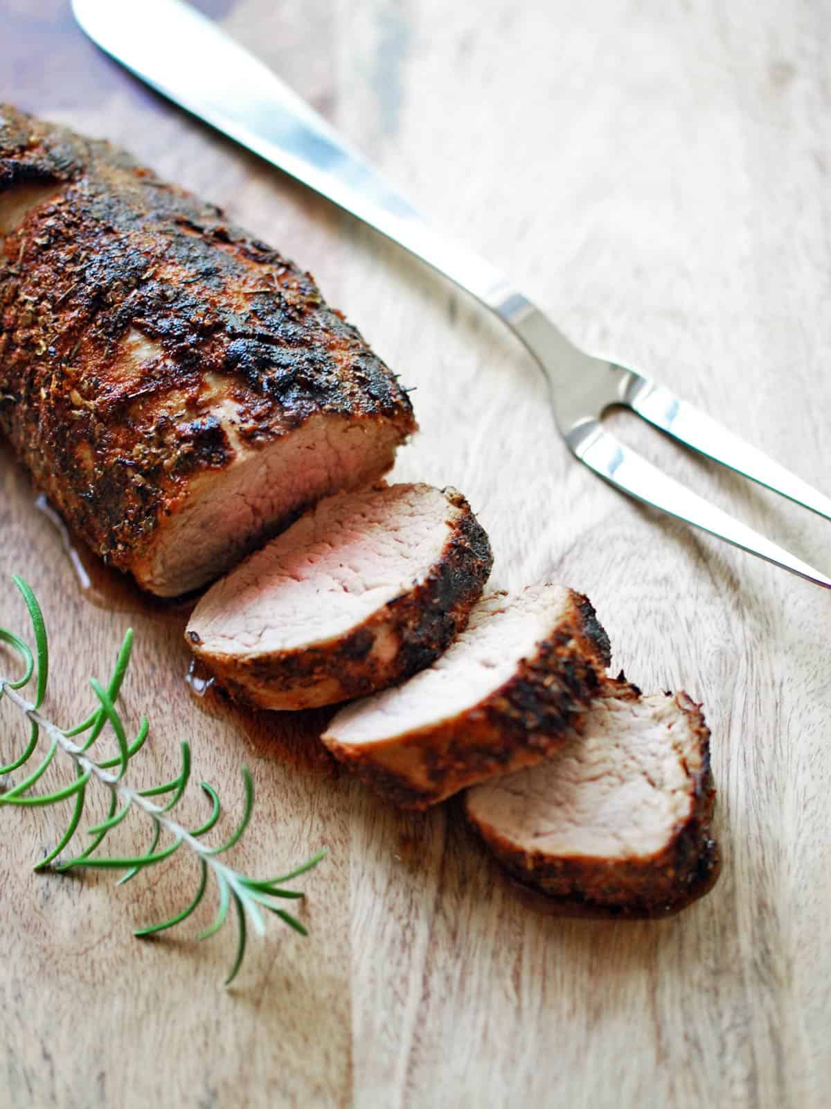 Roasted pork tenderloin is served on a cutting board. 