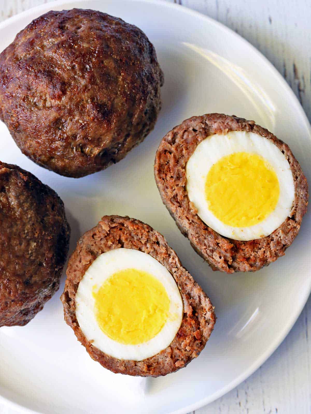 Baked Scotch eggs are served on a white plate.