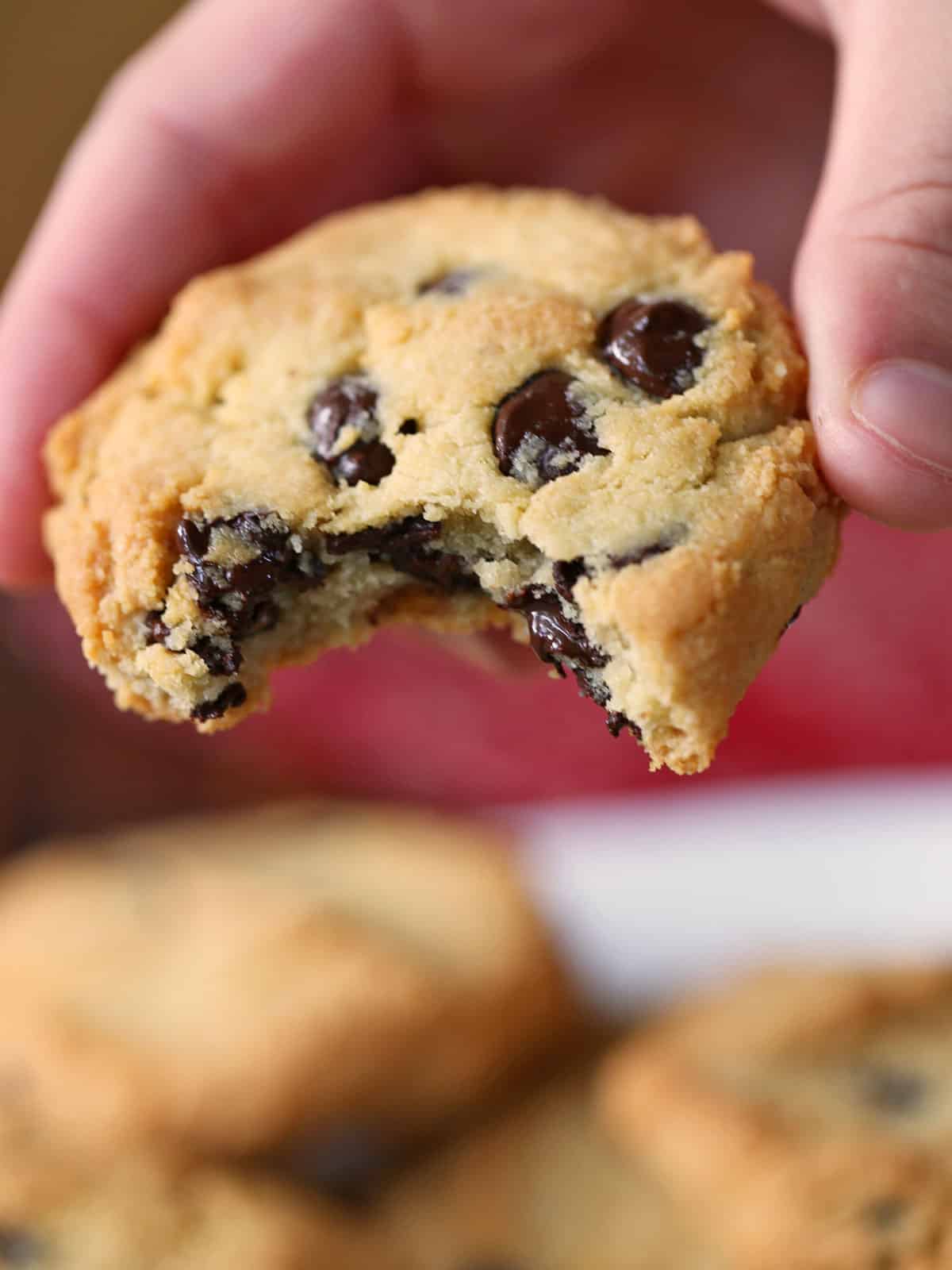 A hand is holding a bitten almond flour chocolate chip cookie.