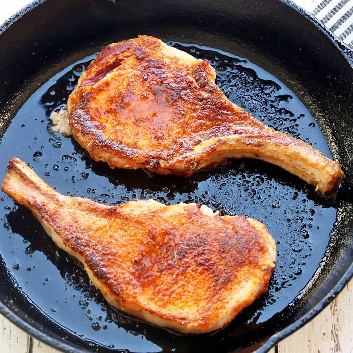 Two thin pork chops in a cast-iron skillet.