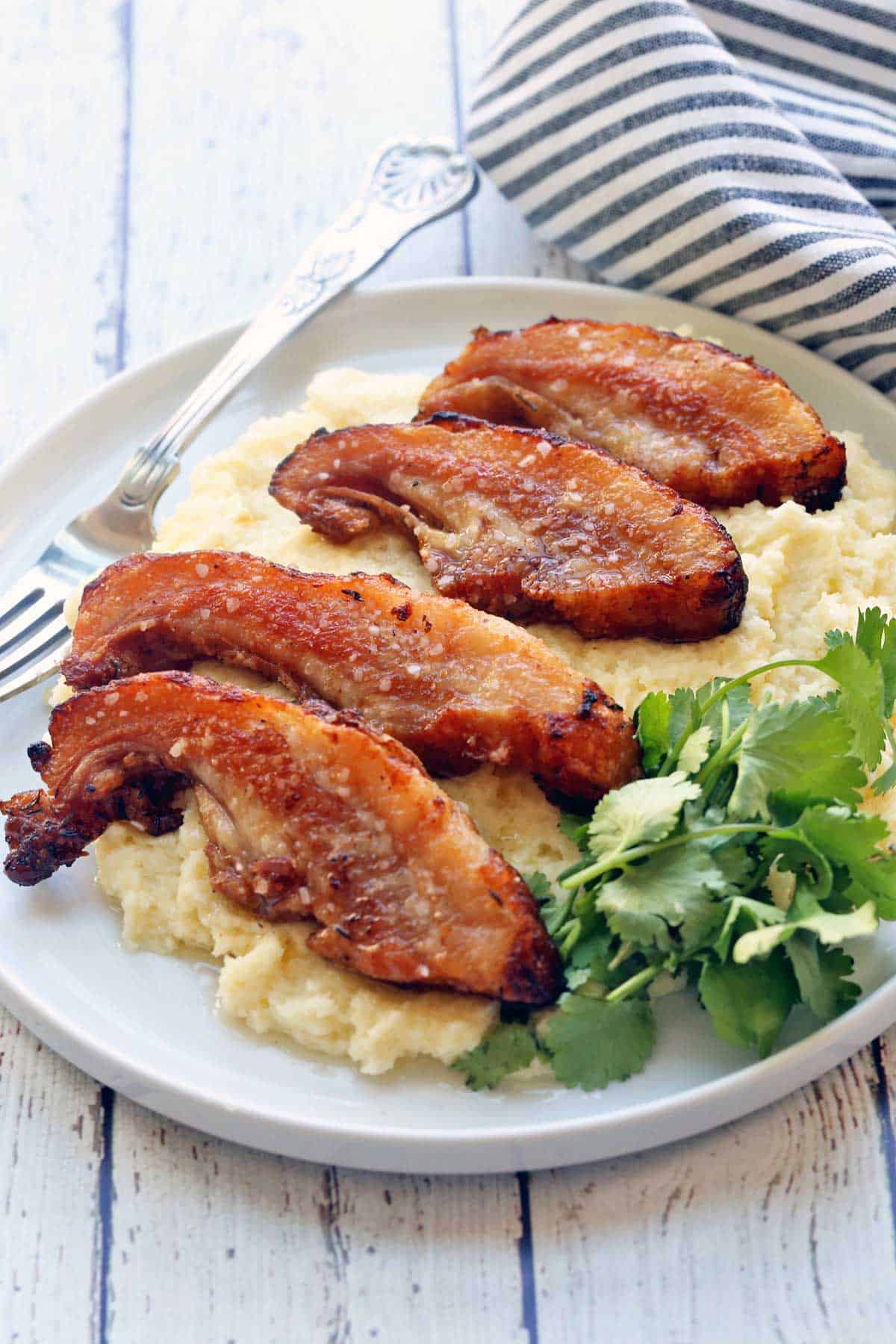 A sliced pork jowl is served on a bed of mashed cauliflower with a fork. 