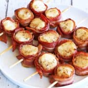 Bacon-wrapped scallops are served on a white plate.