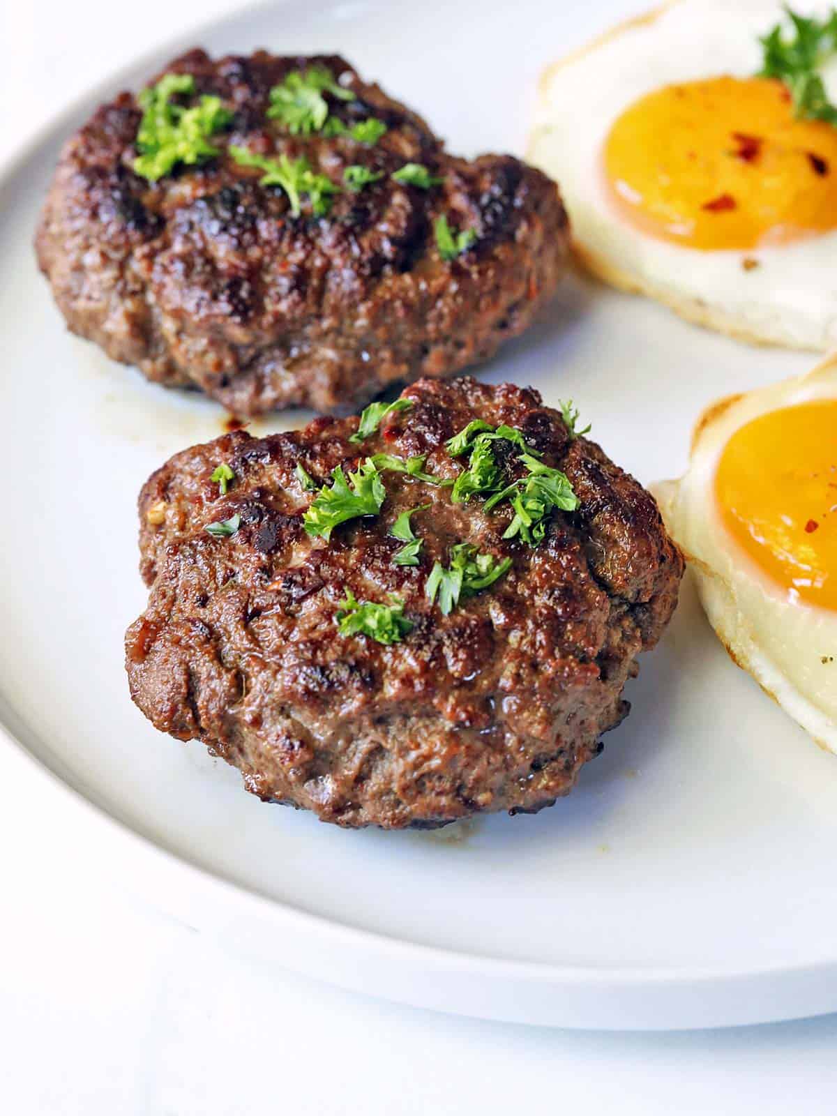 Two beef sausage patties are served with fried eggs. 