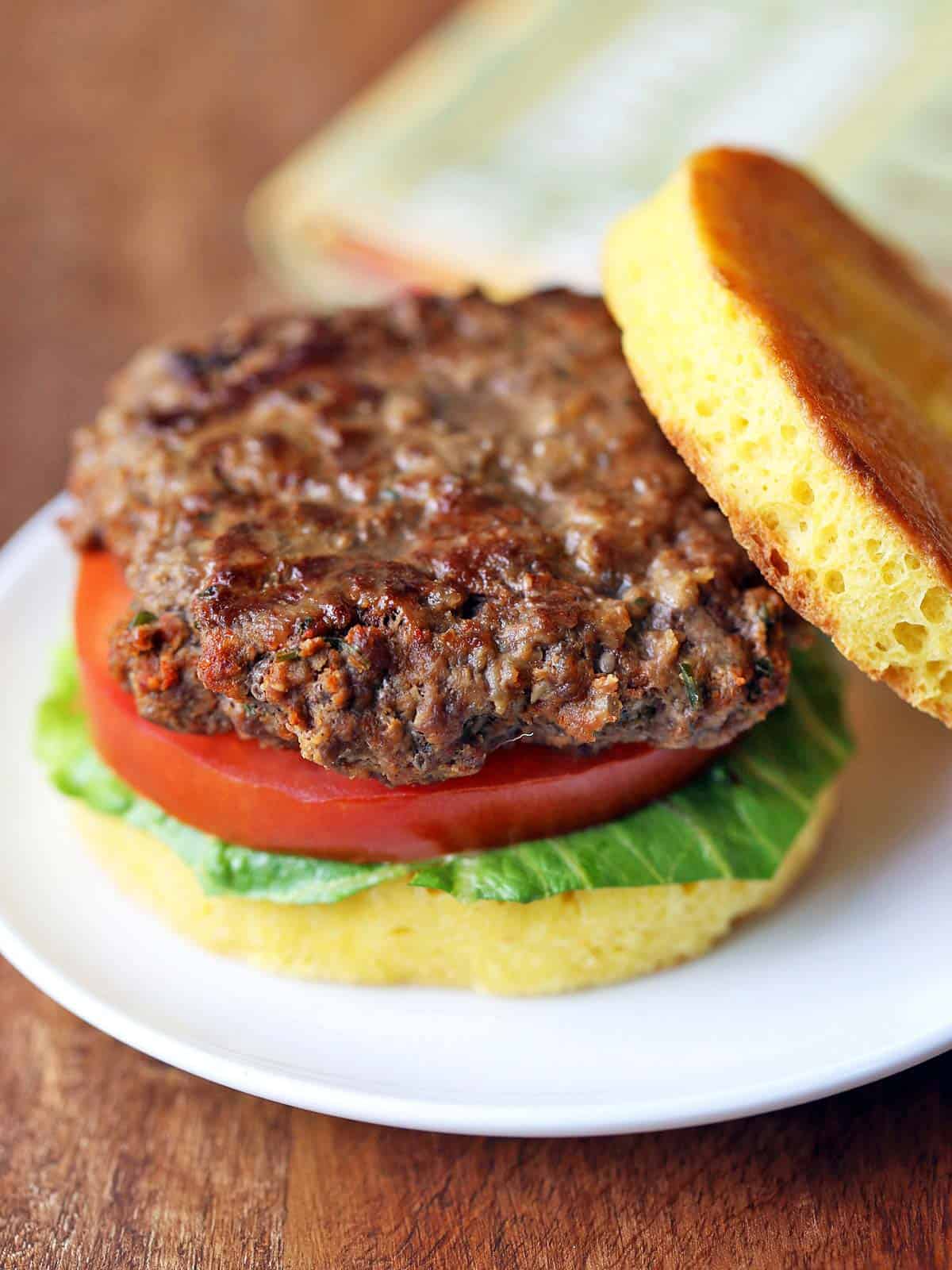 A bison burger is served in a bun with lettuce and tomato.