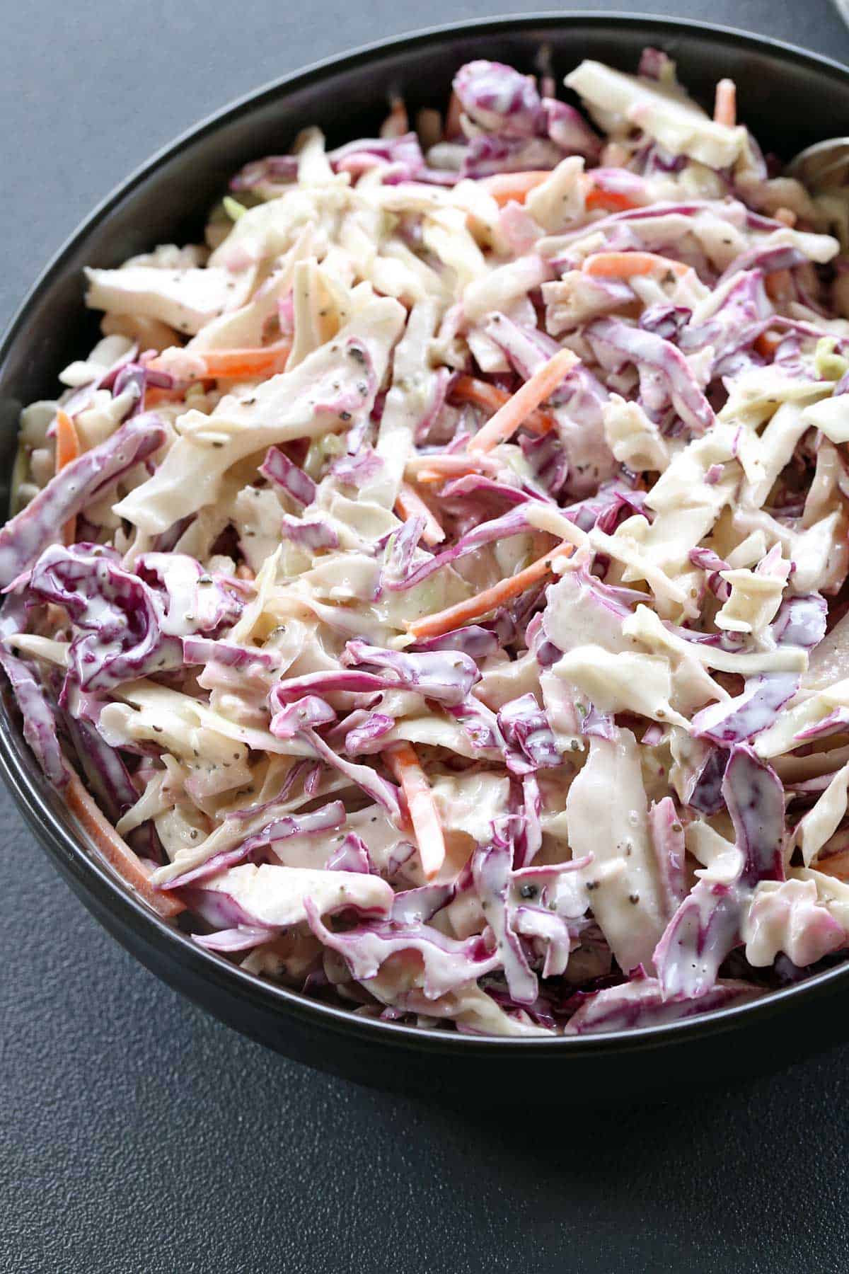 Homemade coleslaw is served in a dark bowl. 