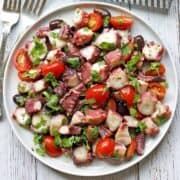 Octopus salad is served on a white plate with forks and a napkin.