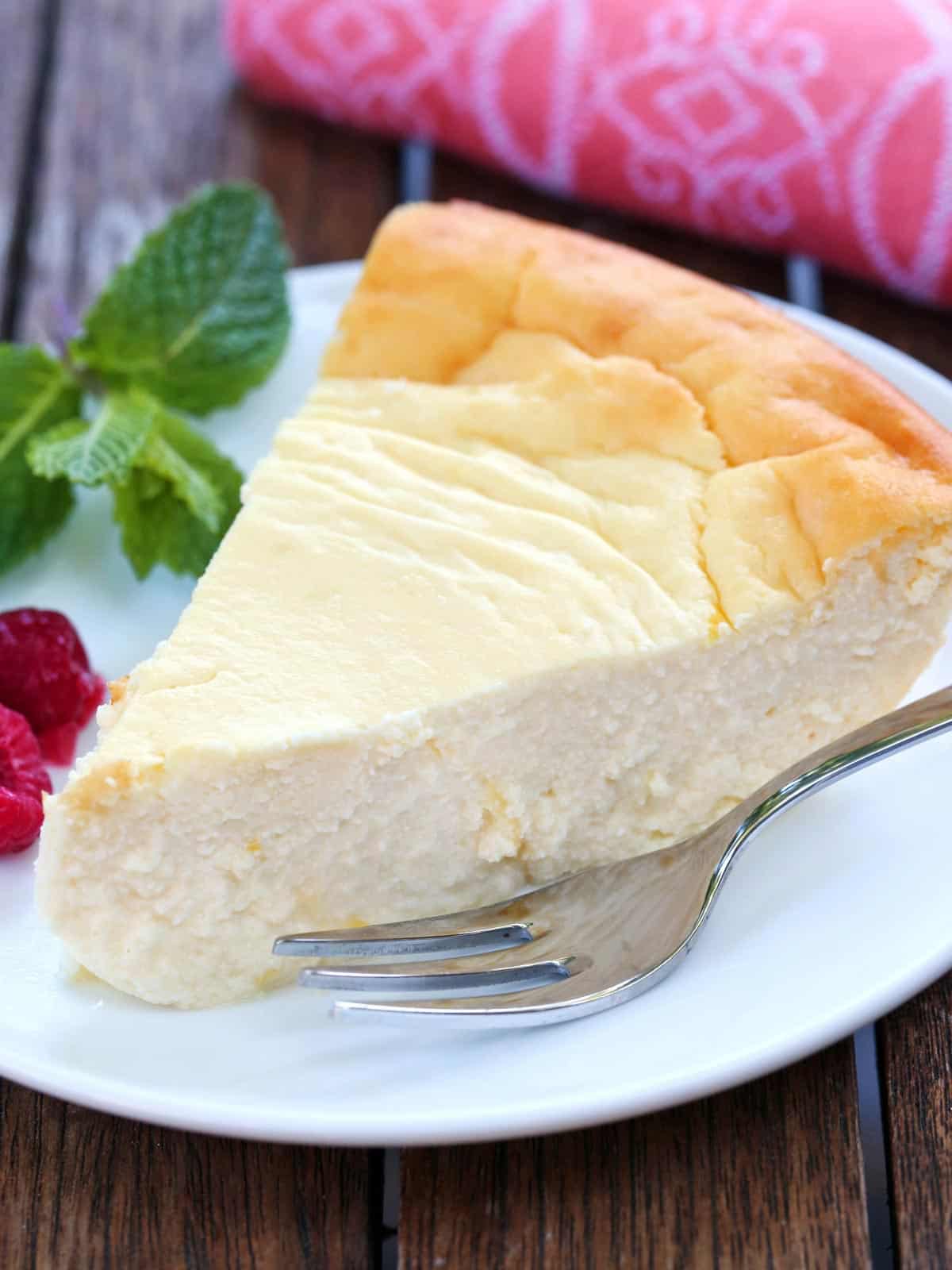A slice of ricotta cheesecake is served on a white plate with a fork.