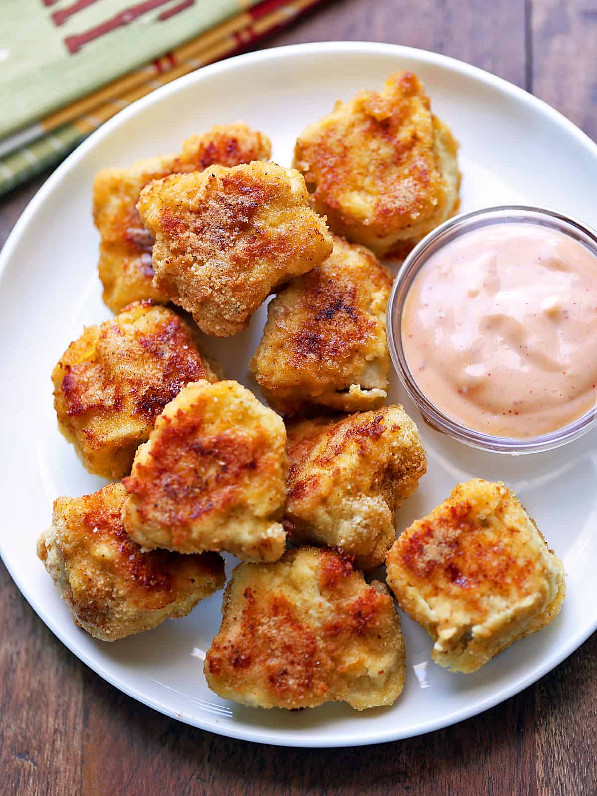 Keto chicken nuggets served on a white plate with a dipping sauce.